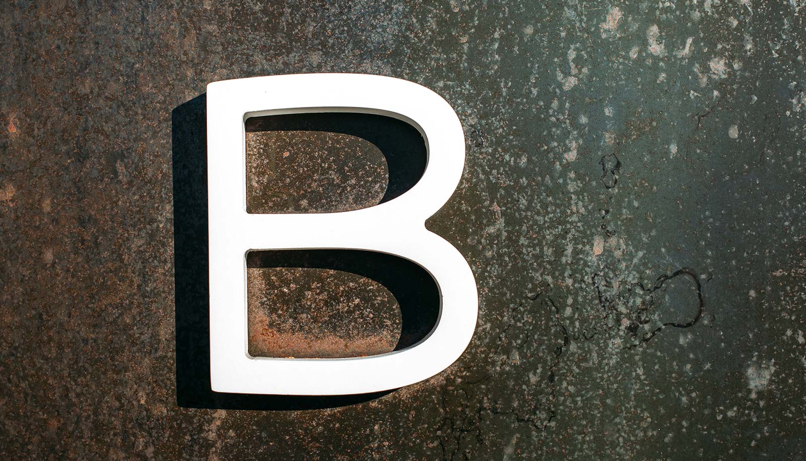 A white letter B on a dark metal surface.