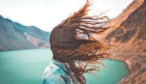 A woman's hair blows in the wind as she's standing outside by a lake.