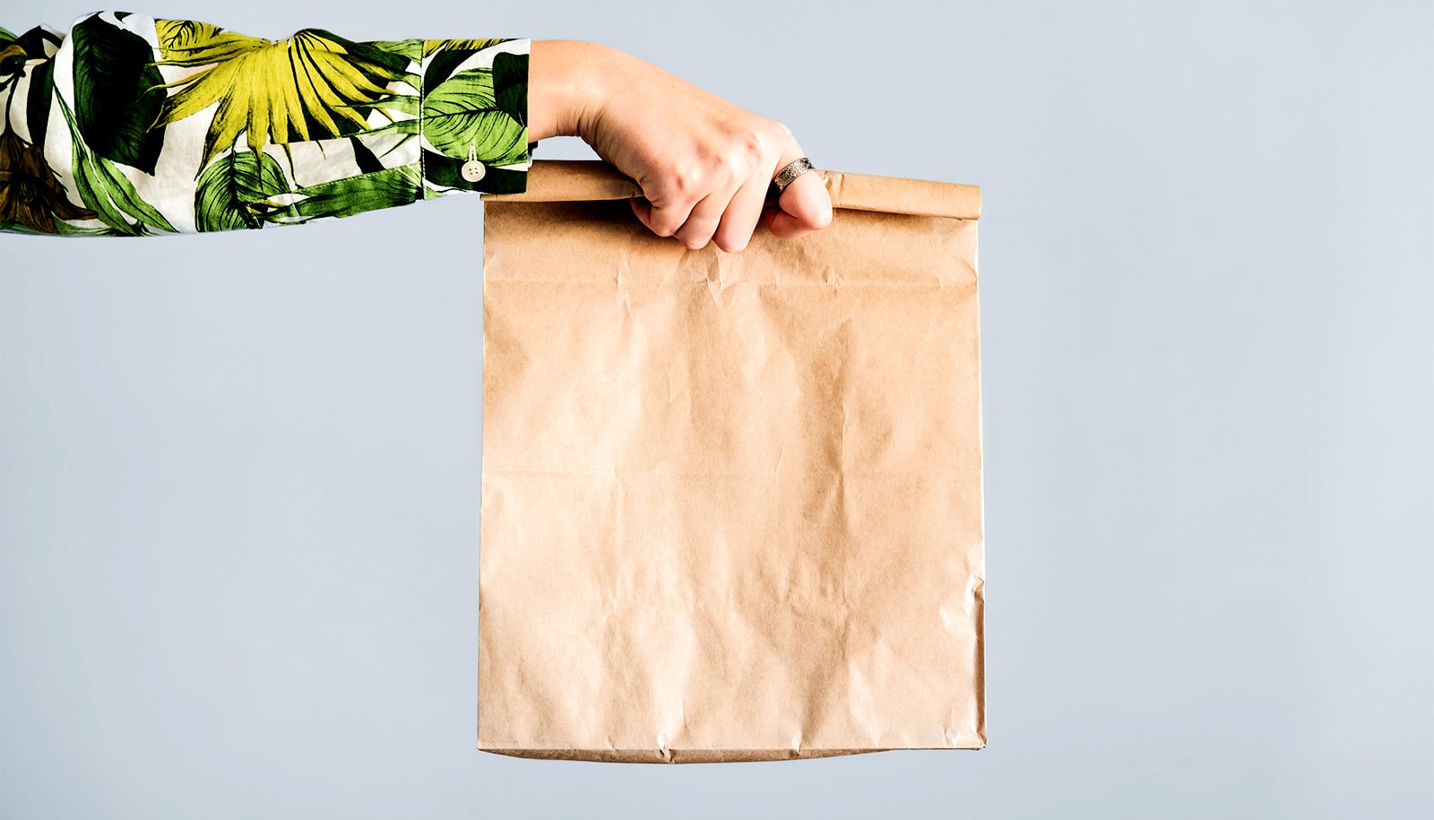A person wearing a shirt with a leafy pattern on it holds a paper bag.