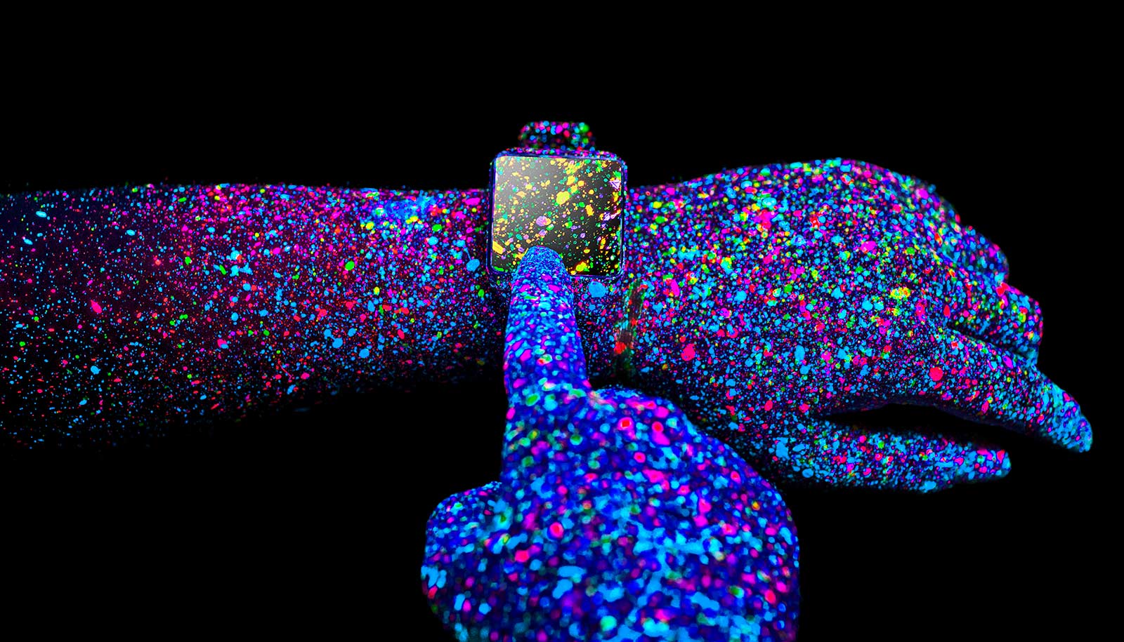 Two hands painted with colorful dots with a smartwatch on one wrist, all against a black background.