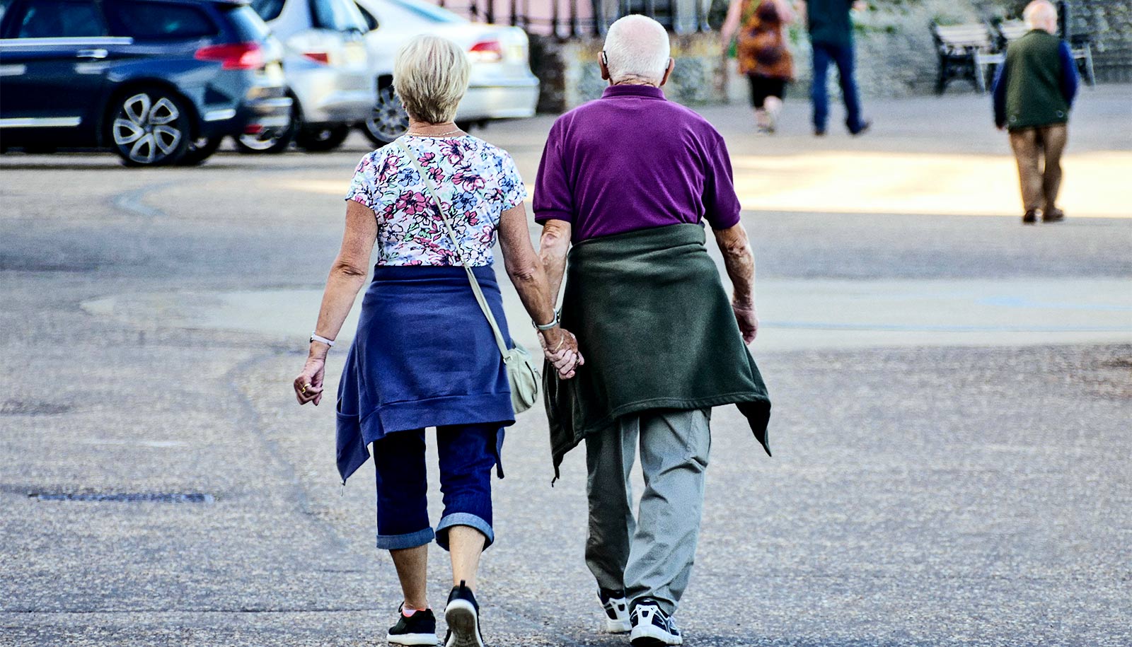An older couple walks in a city together while holding hands.