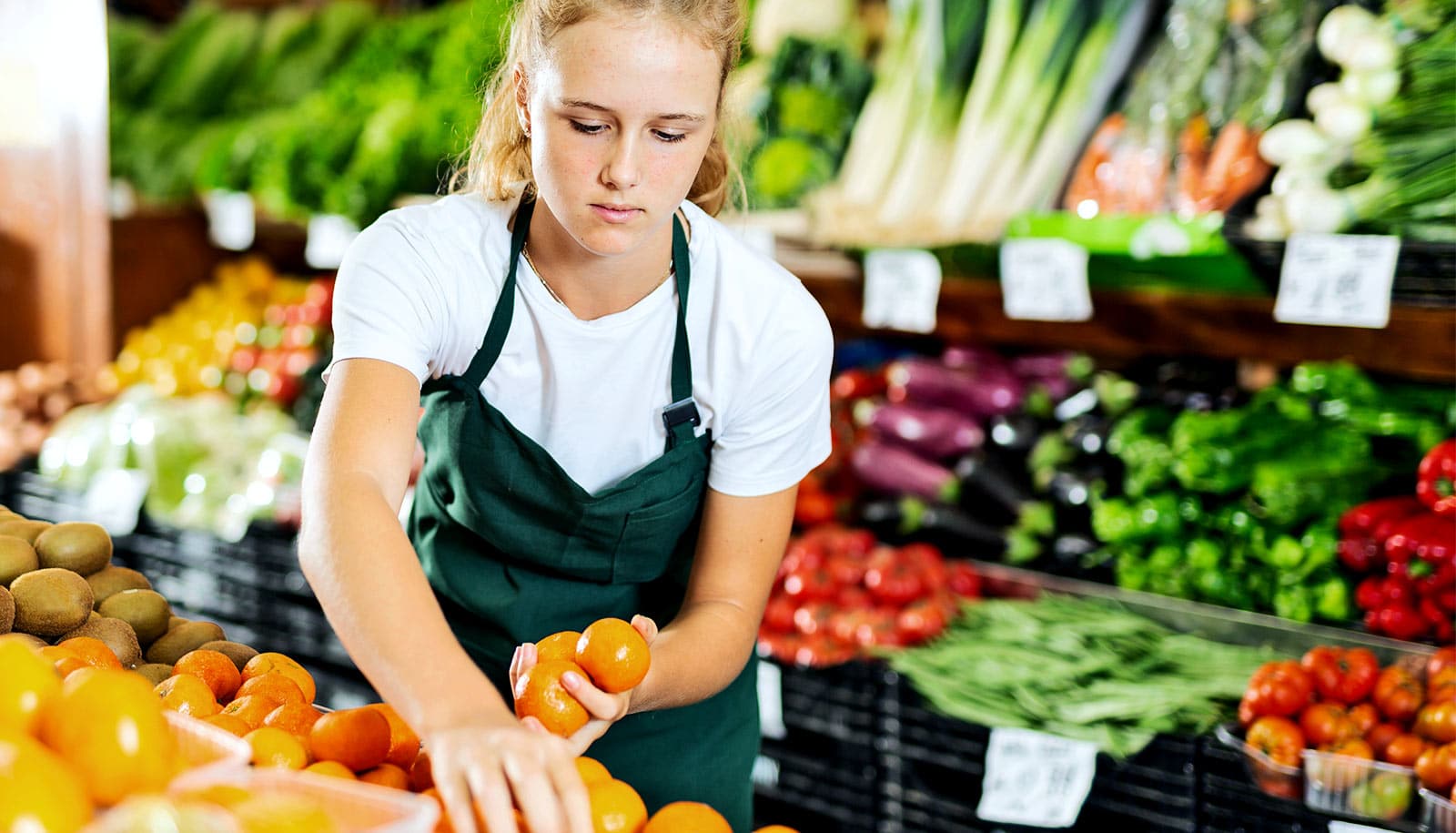 A young woman working as a grocery produce stocker.