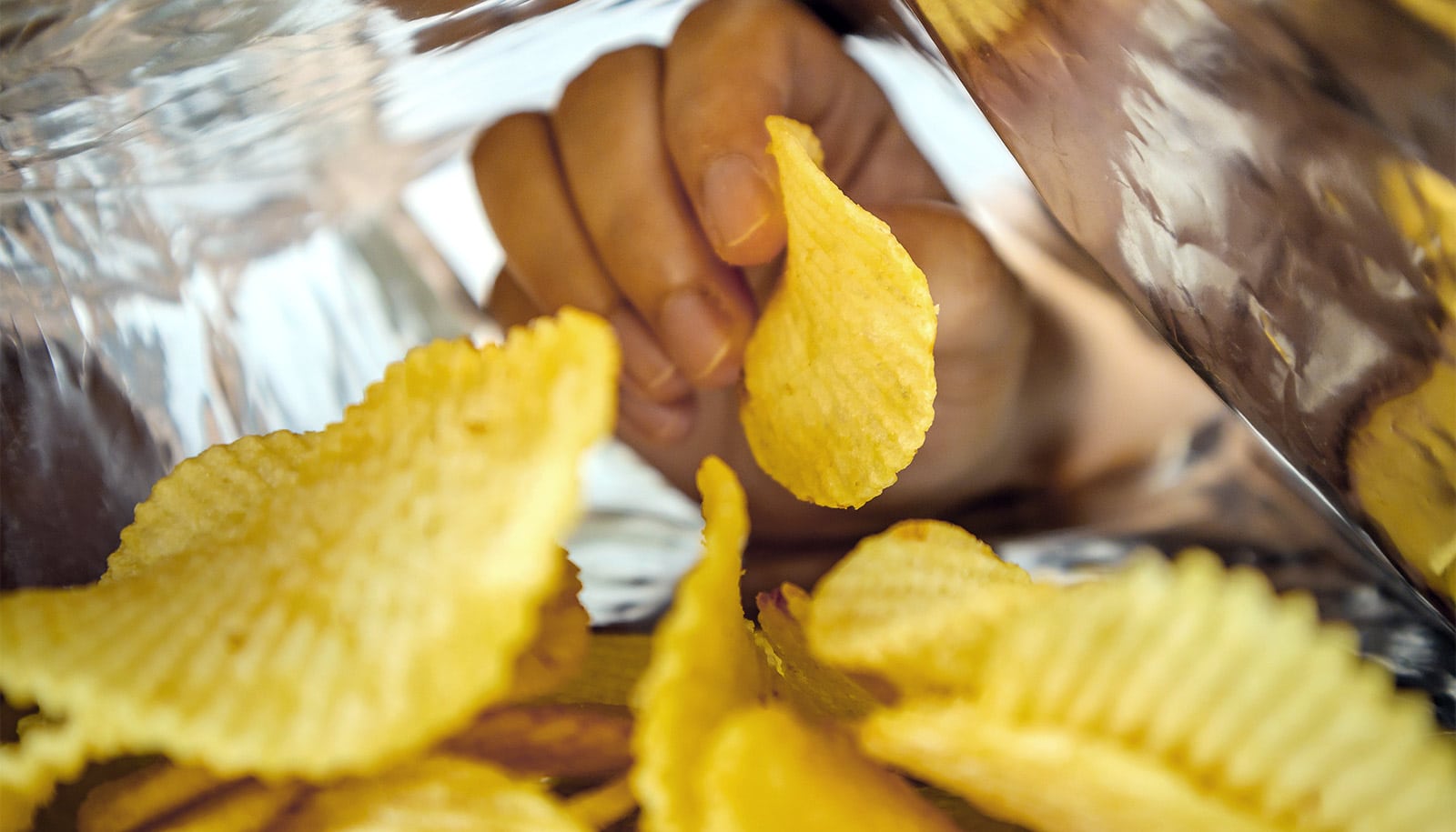 A person reaching into a bag and pulling out a potato chip.
