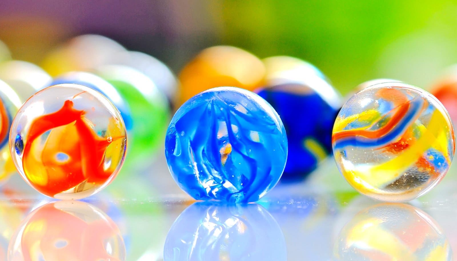 Three glass marbles among a group of marbles sitting on a reflective surface.