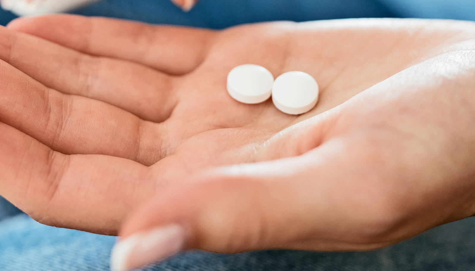 A woman holds two white pills in the palm of her hand.