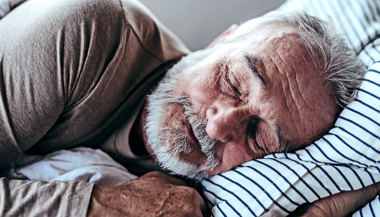 An older man with a white beard sleeps soundly in bed.