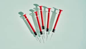 5 red syringes on pale green surface