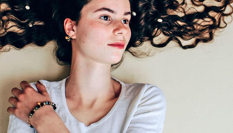 young person lies with outspread long hair, arm across chest on own shoulder