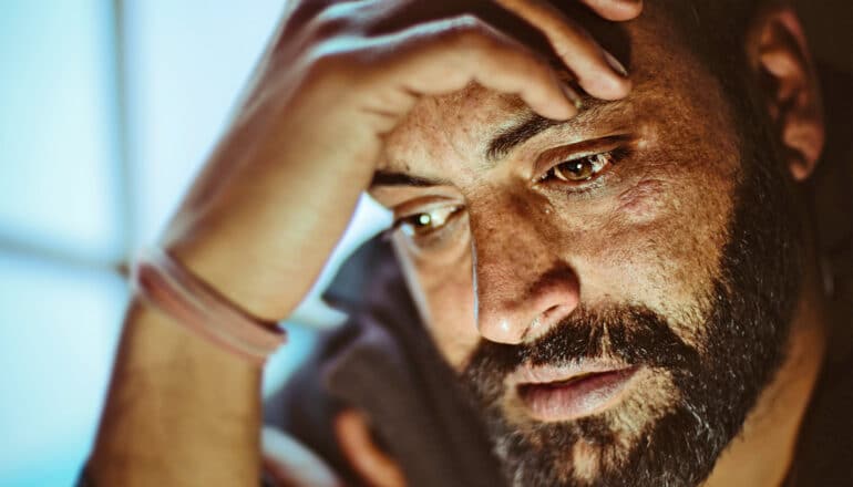 A man cries and rests his head on his hand while looking down.
