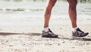 An older man walks on a beach in tennis shoes.