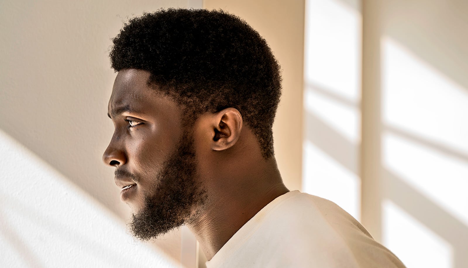 A man looks out a window with a pained expression.