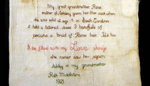 embroidery on cloth reads: "My great grandmother Rose mother of Ashley gave her this sack when she was sold at age 9 in South Carolina it held a tattered dress 3 handfulls of pecans a brain of Roses hair. Told her it be filled with Love always she never saw her again Ashley is my grandmother Ruth Middleton 1921"