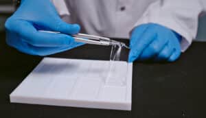 gloved hands hold clear strip over white plastic tray