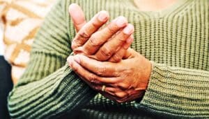 A woman holds one hand with the other in pain.