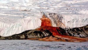red water pours from ice over black rock