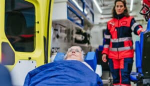 rescuer stands in ambulance as elderly patient enters on stretcher