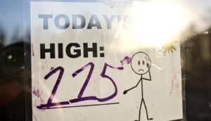 A sign on a window reads "Today's High: 115" and has a stick figure frowning standing under a sun.