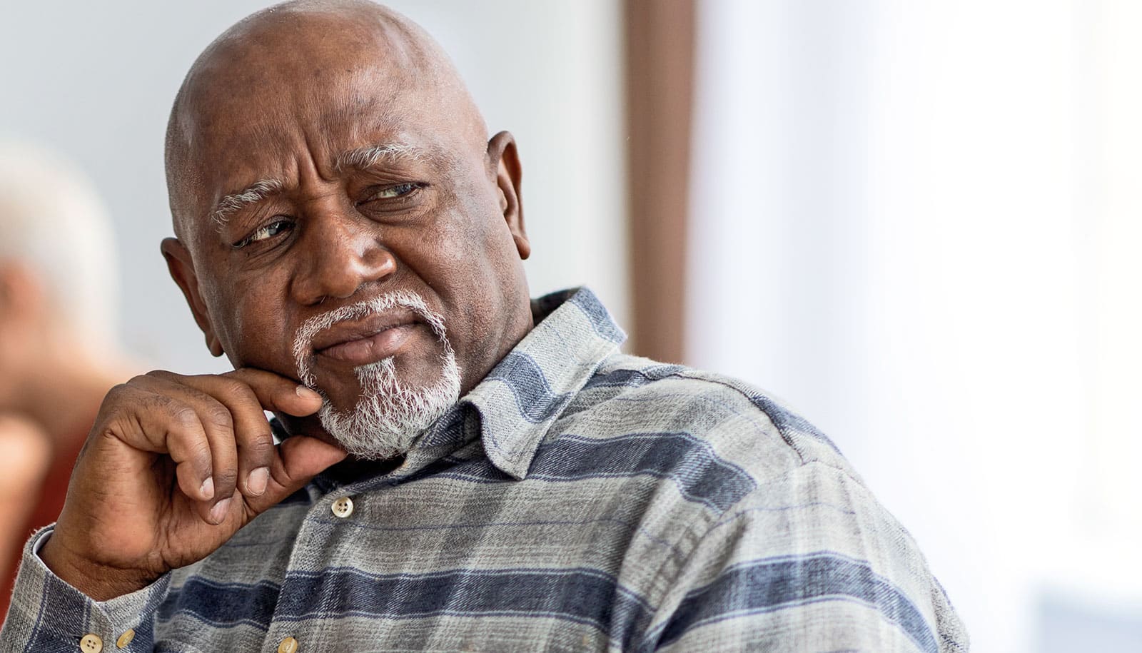 An older man has a frustrated look as he looks out a window.