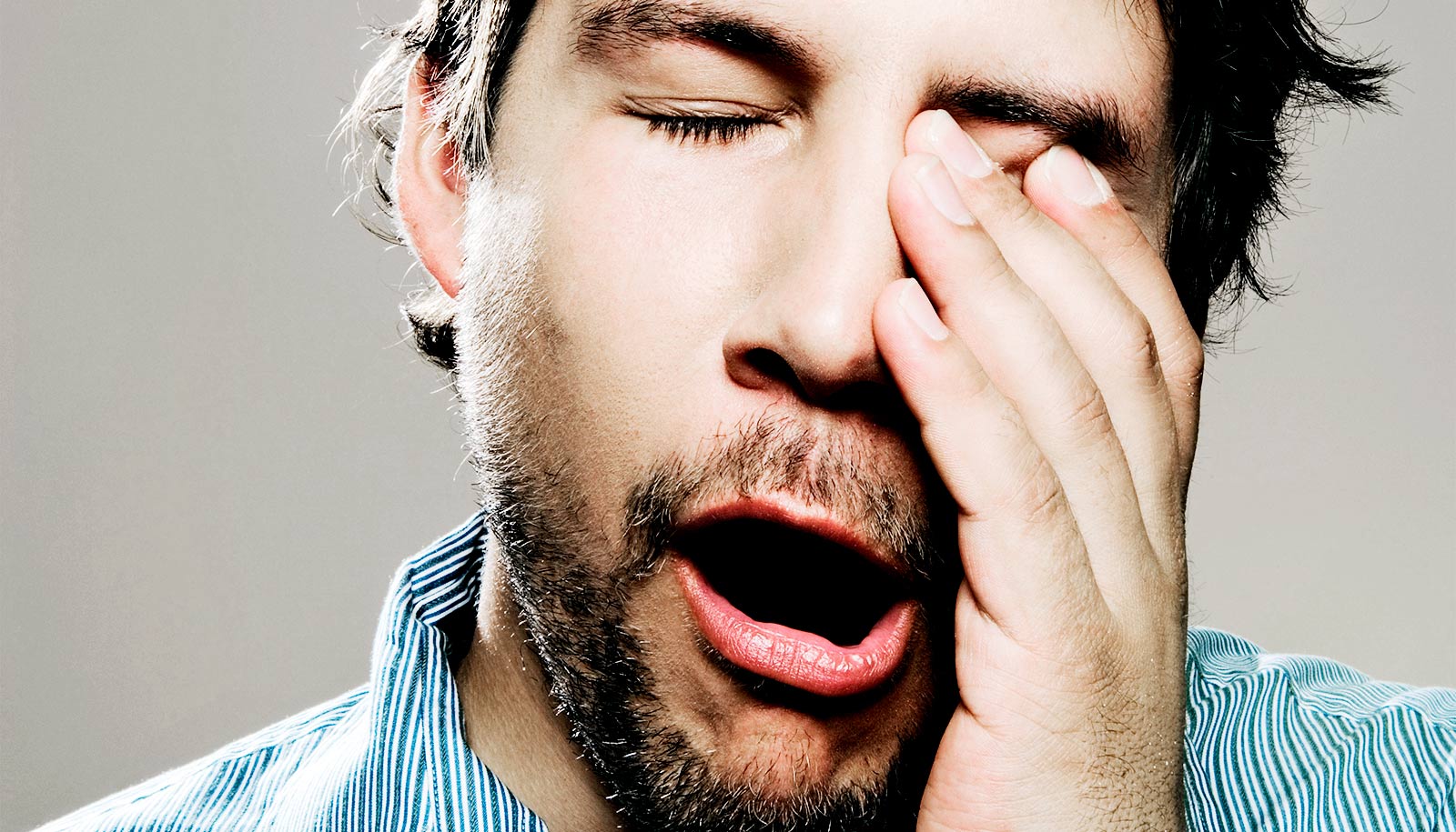 A man yawns and rubs his eye.