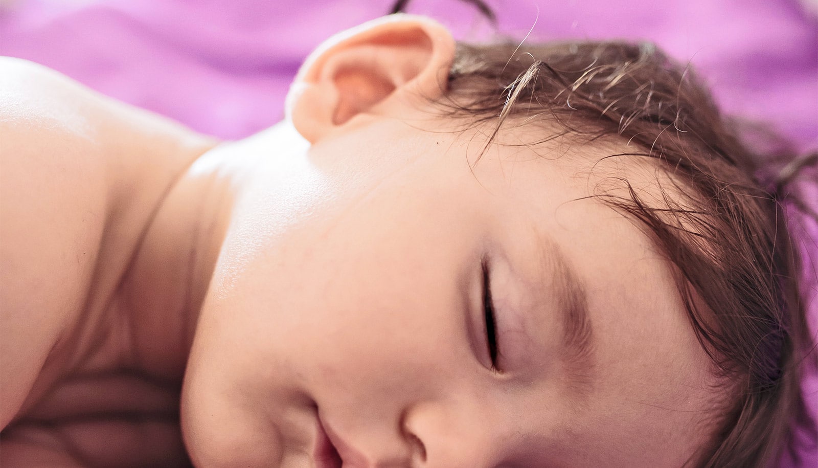A baby sleeps on a bed with purple sheets.