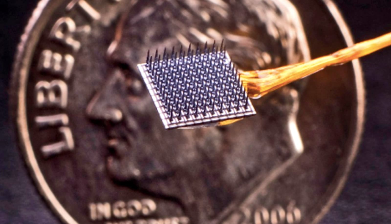 The brain-computer interface implant is a square, spike-covered chip held in front of a penny for scale comparison.