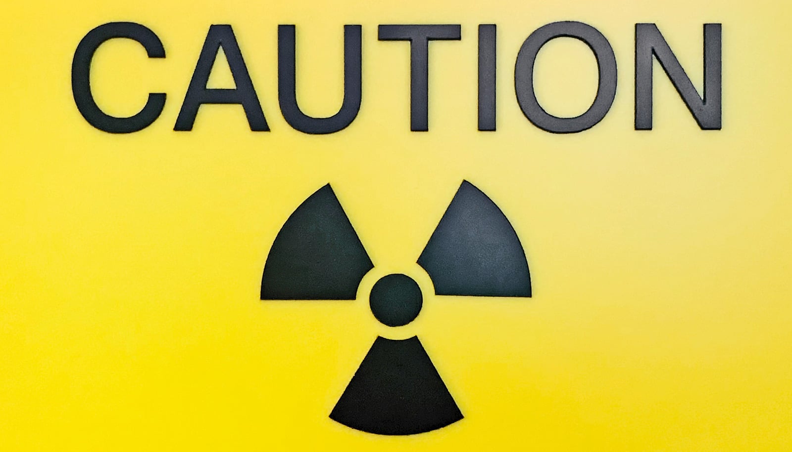 A yellow sign with the word "Caution" on it above a black radiation symbol.