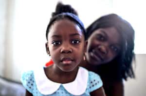 Black mother peeks from behind child in dress