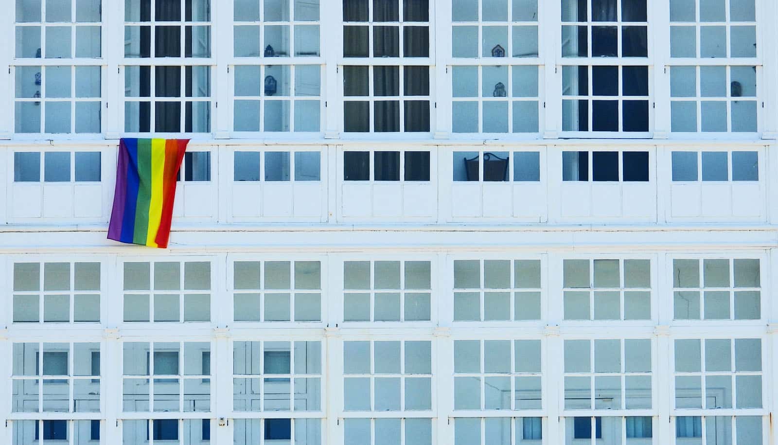 rainbow flag hangs from window of white building