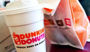 A cup of Dunkin coffee next to a bag with food in it.