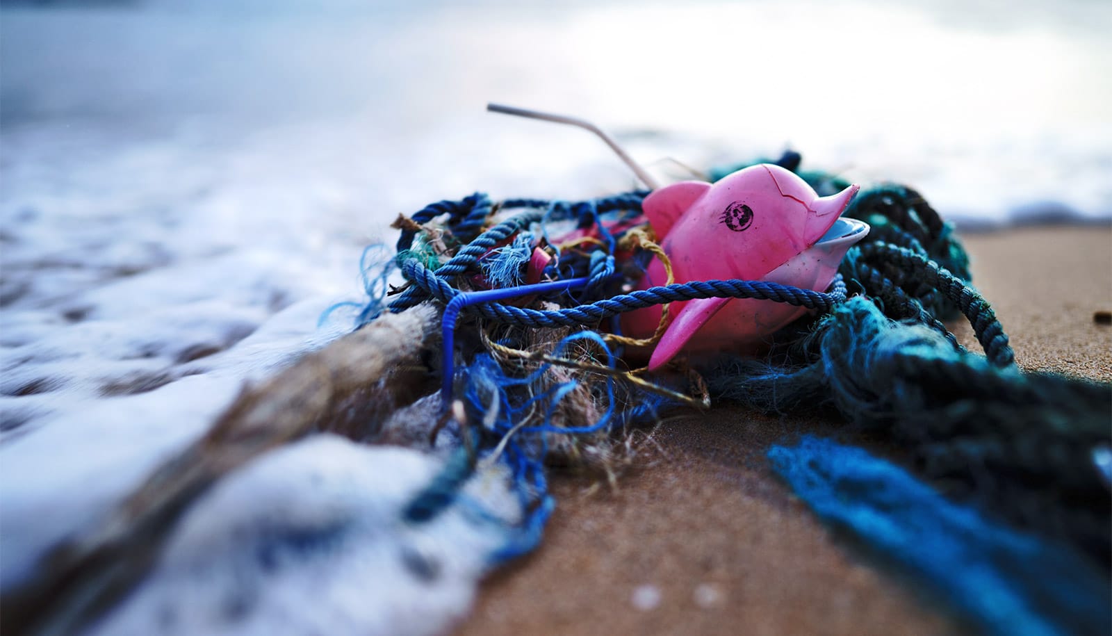 A plastic dolphin among other trash on a beach.