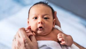 A baby looks up at the camera while being held by a parent.