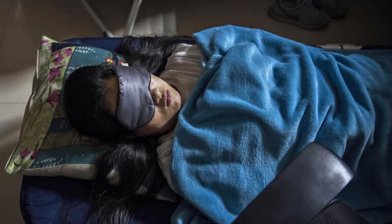person sleeps on cot with eye mask and blanket