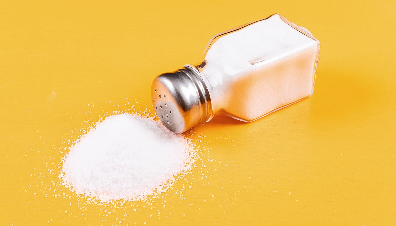 A salt shaker spilled on a yellow surface.