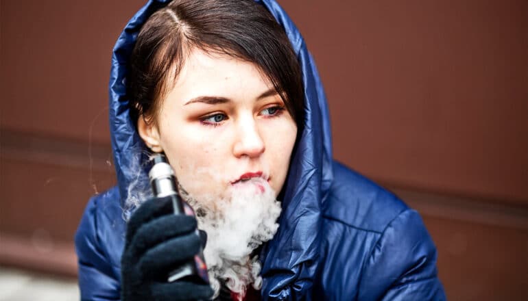 A young woman vapes outside.