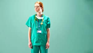 A female doctor in scrubs stands alone against a green background.