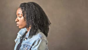 A sad-looking woman in a jean jacket looks downward.