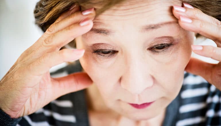 An older woman holds her head with both hands and looks down.