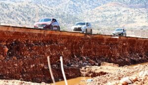 Three cars drive on a road on top of eroded earth.