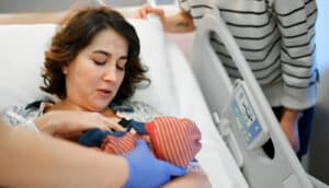 gloved hands hold newborn to mother's breast in hospital