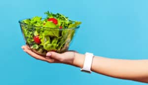 A woman holds a large salad against a blue background.