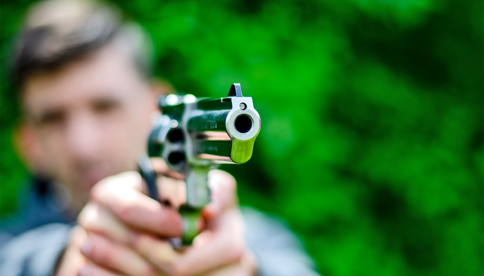A young man aims a handgun while standing outside.