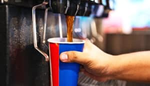 A person fills up a cup at a soda fountain.