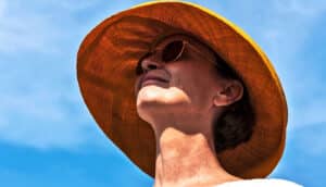 A woman with a large sun hat and sunglasses smiles and looks up.
