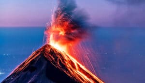 A volcano spits lava at dusk.