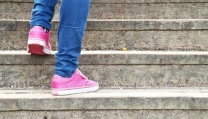 A person in blue pants and pink sneakers walks up concrete stairs.