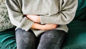 A woman sits on a couch holding her stomach in pain.