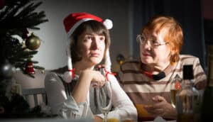 adult in christmas hat rolls eyes next to older adult at dinner table
