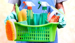 A man holds a basket filled with cleaning supplies.