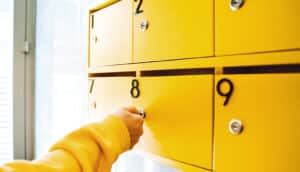 A woman in a yellow sweater opens a yellow apartment mailbox.