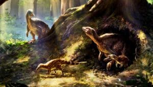 An adult dinosaur emerges from a hold beneath a tree with younger dinosaurs and see another dinosaur coming over a ridge in the background.